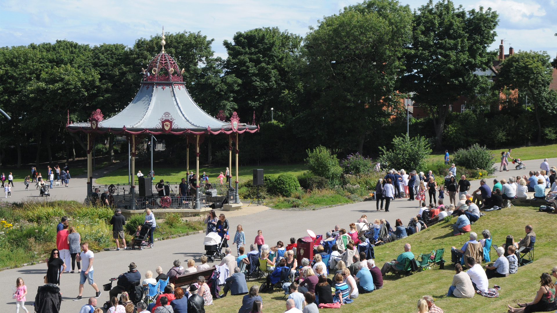 People gathered on a grassy hill, watching a performance on a band stand