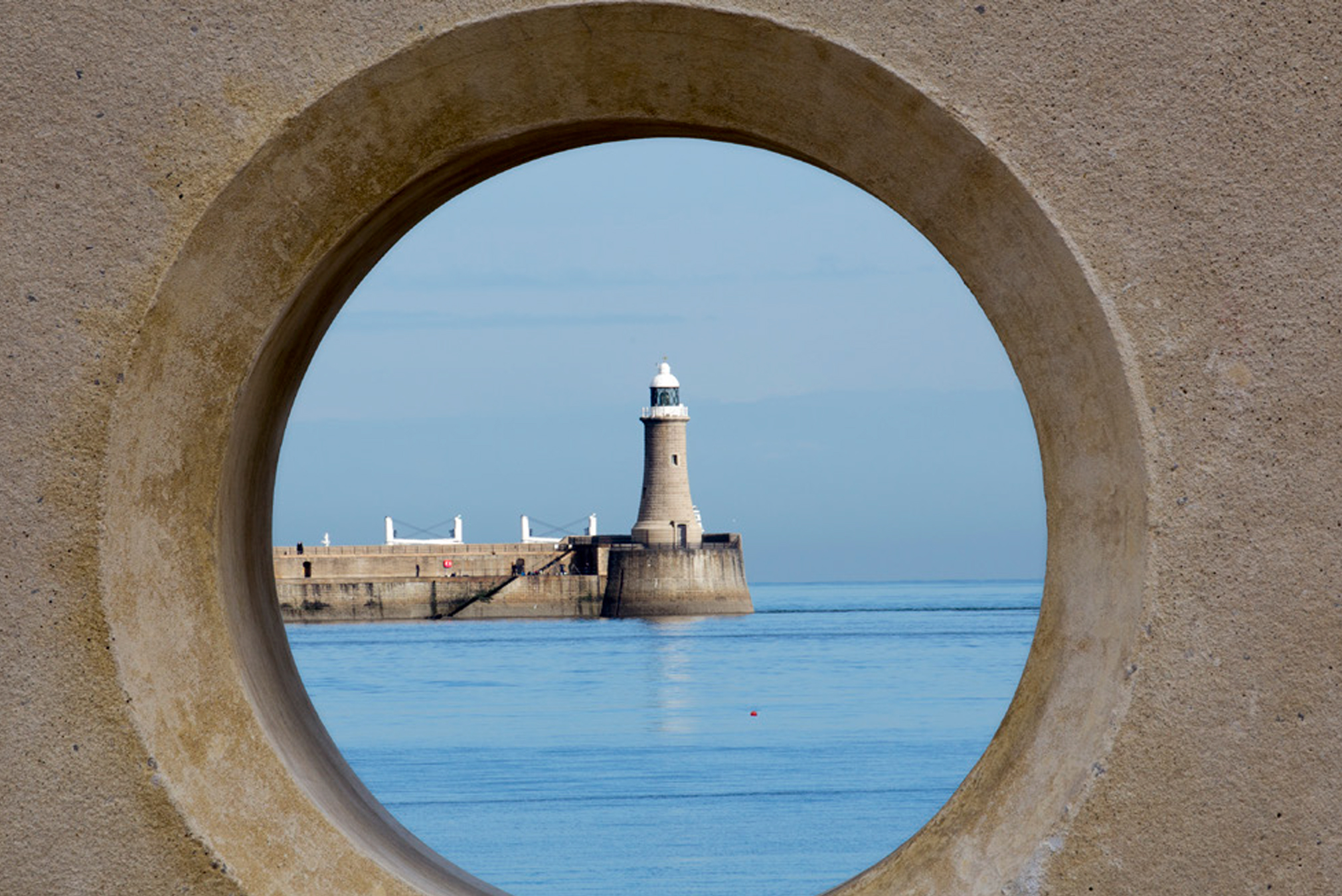 A lighthouse through a stone viewing area