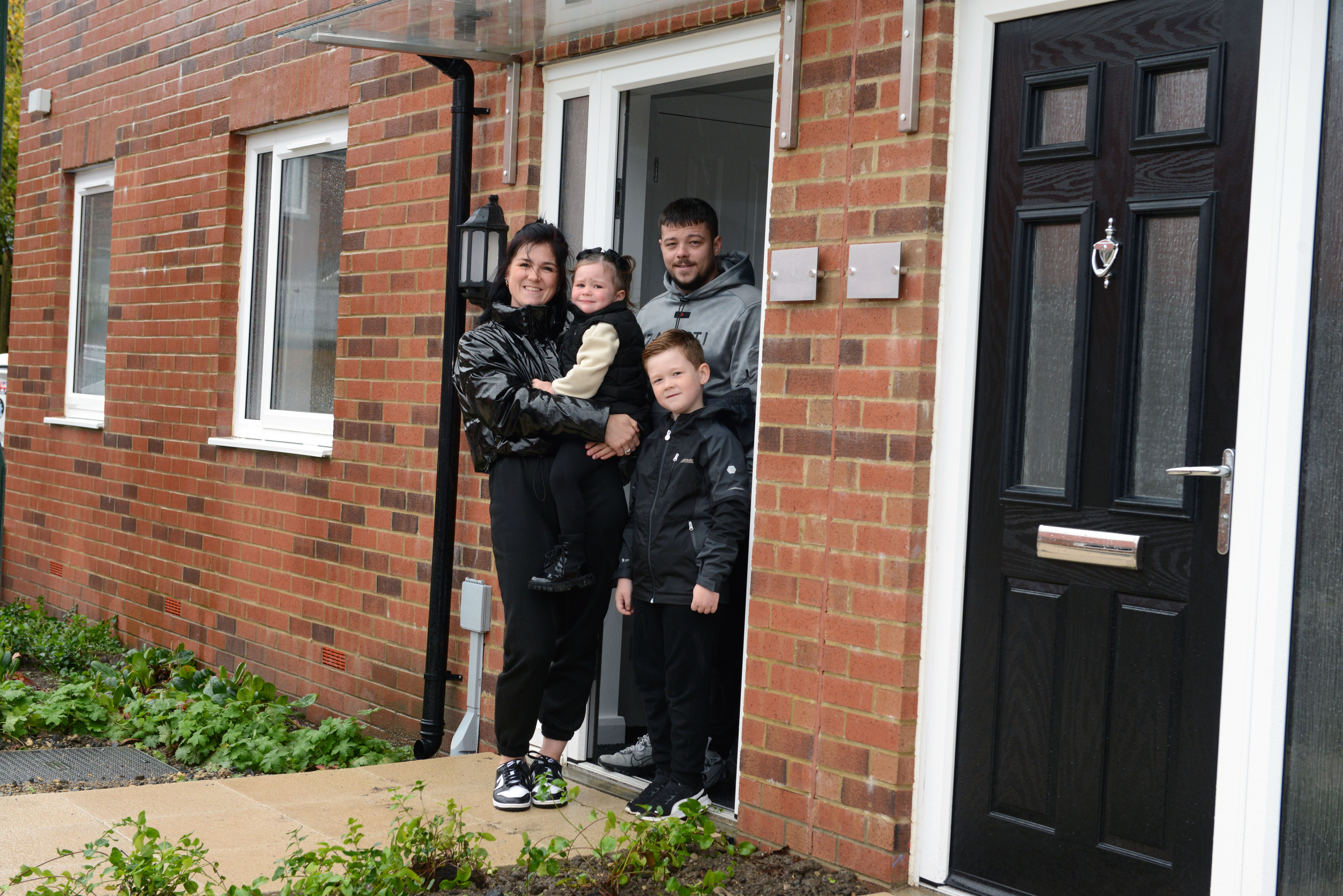 Young family stood in front door of new home.