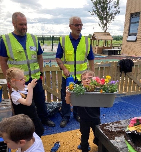 Two adults helping children to plant flowers in pots.