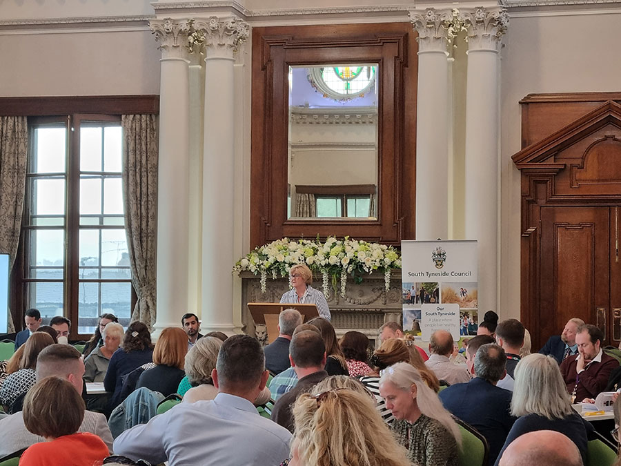 A woman talking to a large group of people in the Town Hall