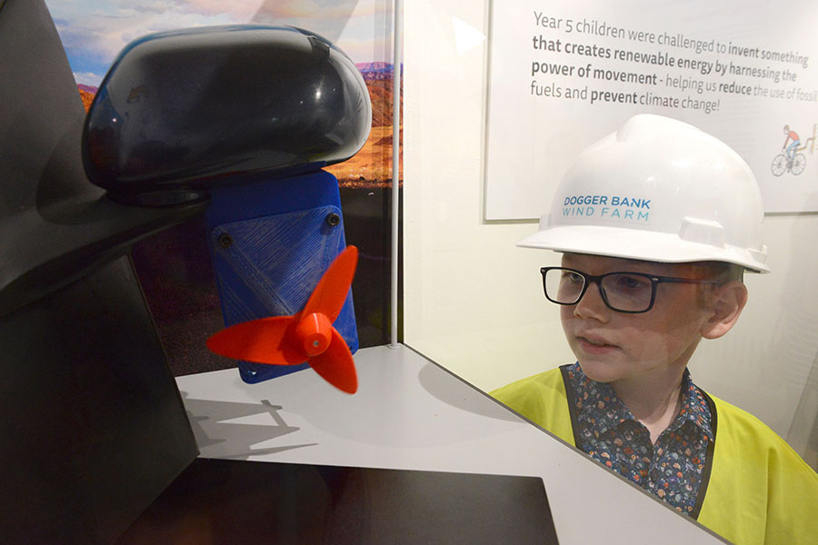 Child wearing a hard hat, who is looking at a turbine.