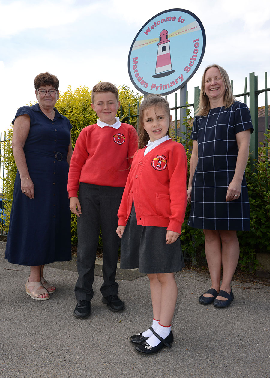 Two children, in school uniform, stood outside the school gates with a Headteacher and a Councillor.