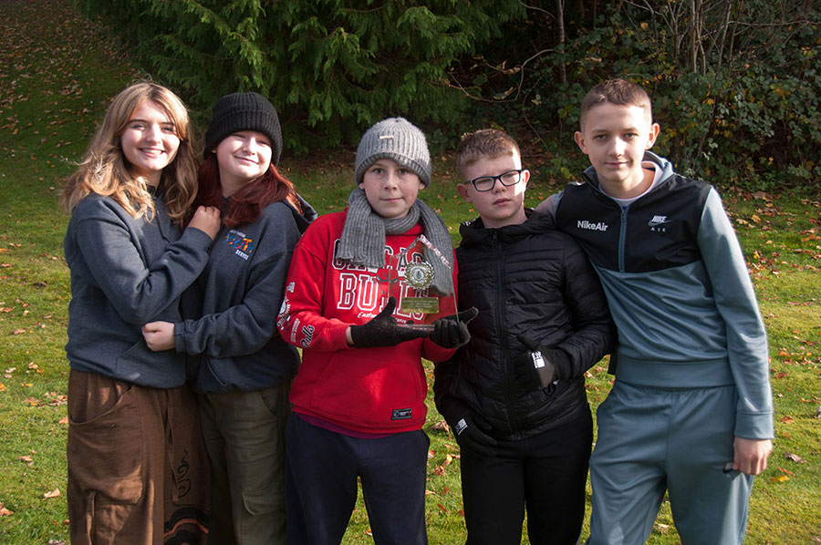 Five people outdoors, holding a trophy.