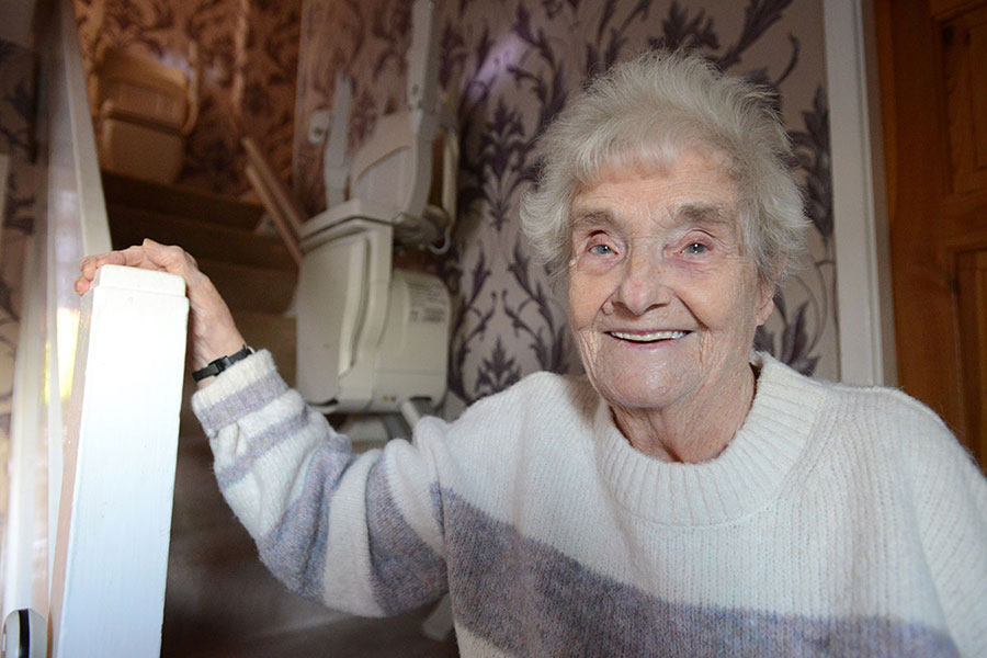 A person standing in their home, near a staircase with a stairlift.