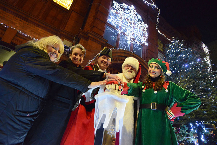 A group of people in festive attire standing in front of a decorated building illuminated with Christmas lights.